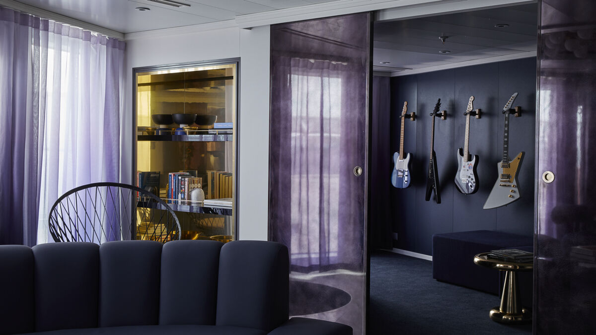 A RockStar Quarters suite living room aboard a Virgin Voyages ship, with a hanging chair and a wall of electric guitars