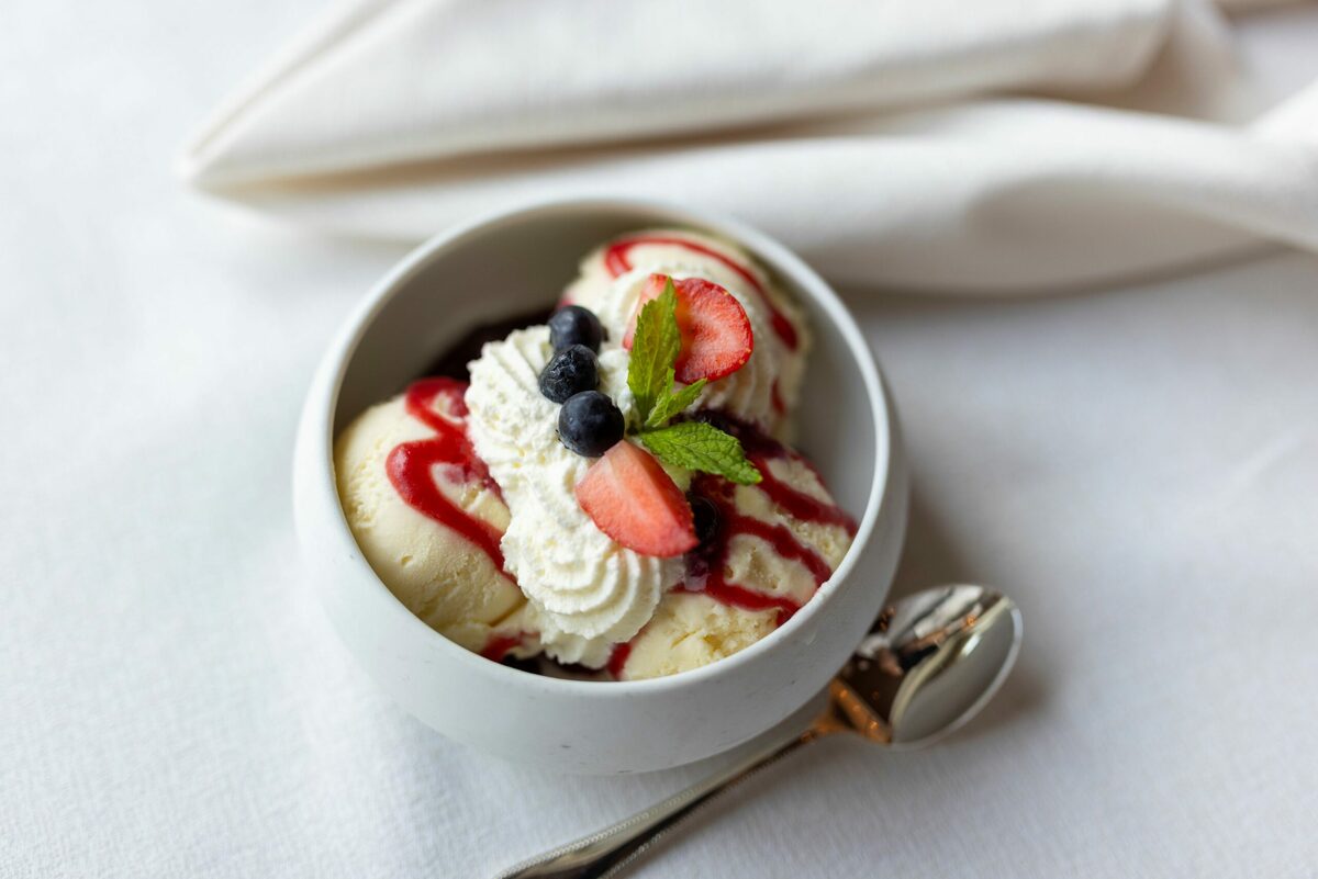 A bowl of vanilla ice cream drizzled with berry sauce, topped with whipped cream, fresh berries and mint