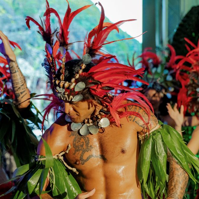 A Polynesian dancer in a feathered headdress and leafy costume performs in French Polynesia