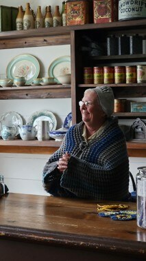 A costumed interpreter stands behind the counter of a recreated period general store